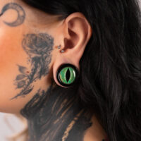 Verena Venus Plug mit grünem Katzenauge Großer grüner Katzenaugen-Plug im Ohr einer tätowierten Person