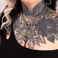 Silberne Herz-Choker-Kette mit Tattoo-Hintergrund Silberne Choker-Kette mit herzförmigem Anhänger auf tätowierter Haut