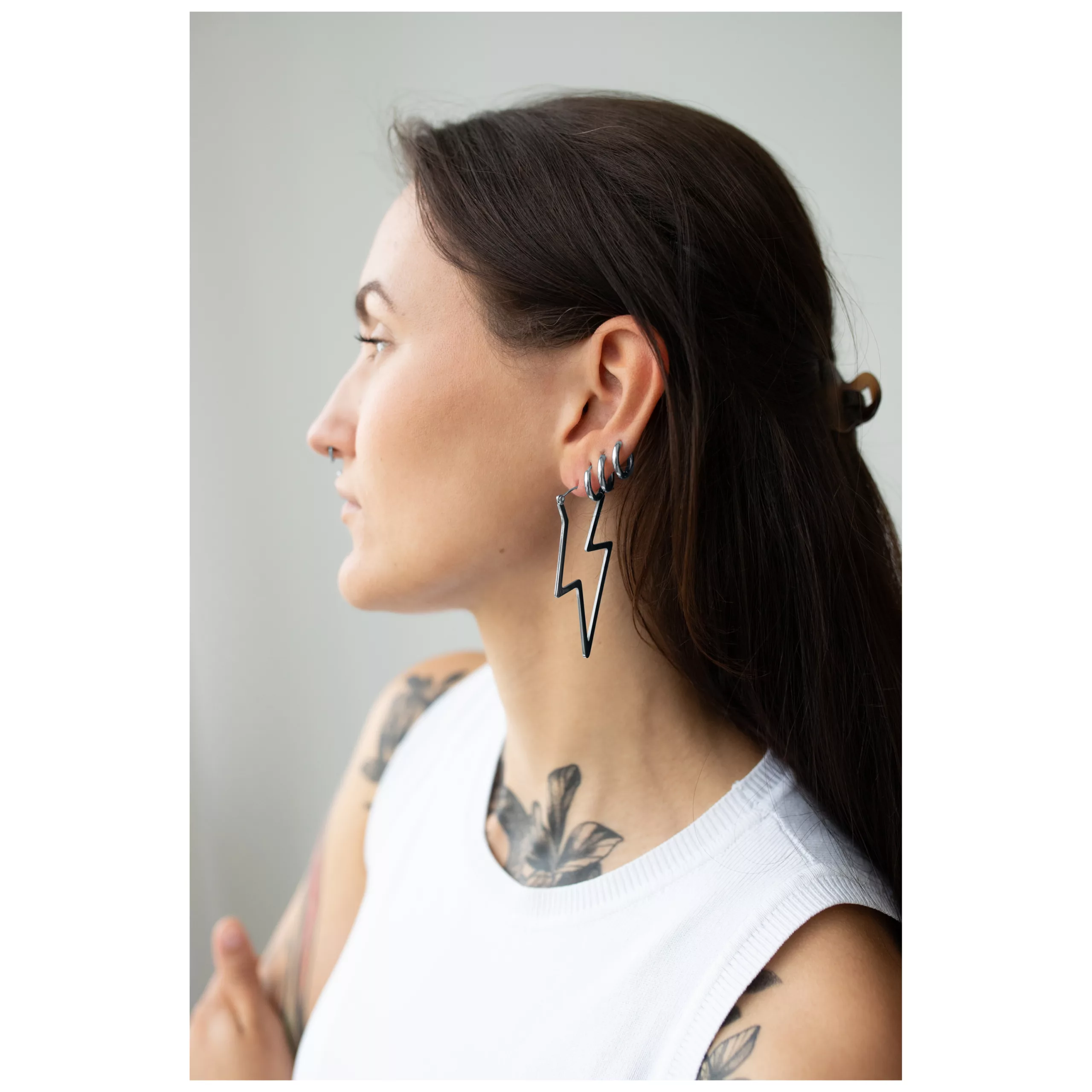 Stylische Thunderbolt Hoops Ohrringe in Schwarz Frau mit langen Haaren trägt schwarze Blitz-Ohrringe aus Stahl, seitliches Porträt