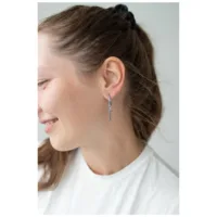 Elegante Little Cross Hoops in Silber Frau trägt silberne Kreuz-Ohrringe, lächelnd im Profil auf hellem Hintergrund