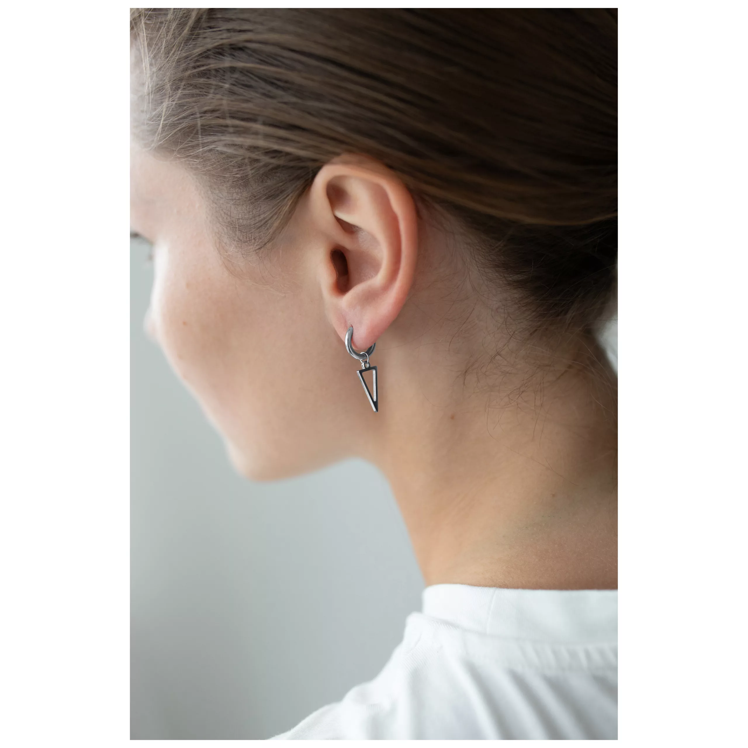 Kleine Dreieck Creolen in Schwarz und Silber Schwarze und silberne Dreieck Creolen am Ohr einer Person mit braunem Haar, weißer Hintergrund