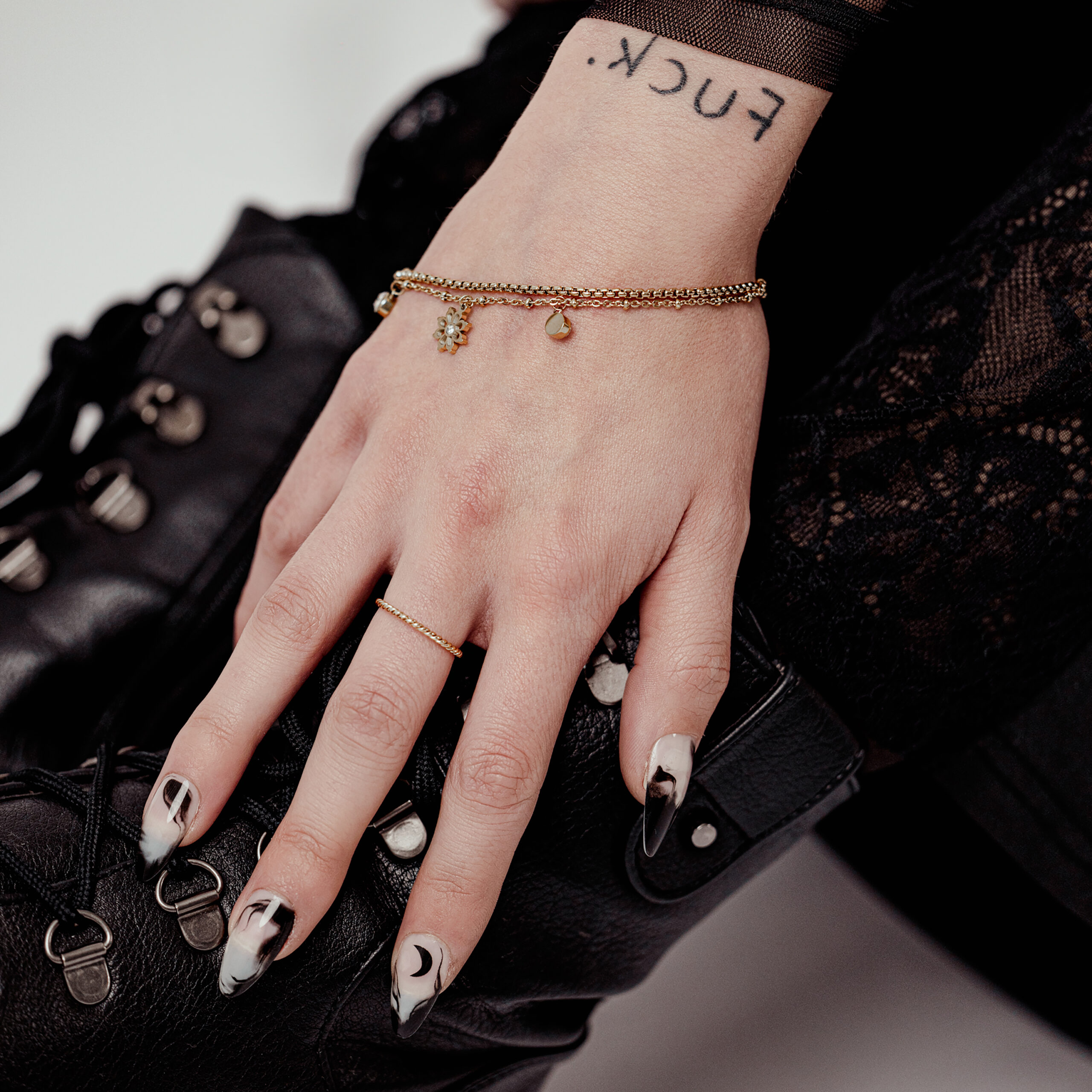 Stilvolles Little Floralis Armband in Gold Hand mit Little Floralis Armband in Gold auf schwarzem Lederstiefel