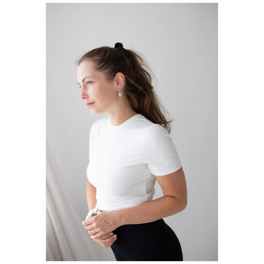 Frau mit weißen T-Shirt und eleganten silbernen Ohrringen vor neutralem Hintergrund