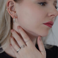 Eleganter Twisted Ring in Silber getragen Frau mit mehreren Ohrringen, die einen silbernen Twisted Ring trägt