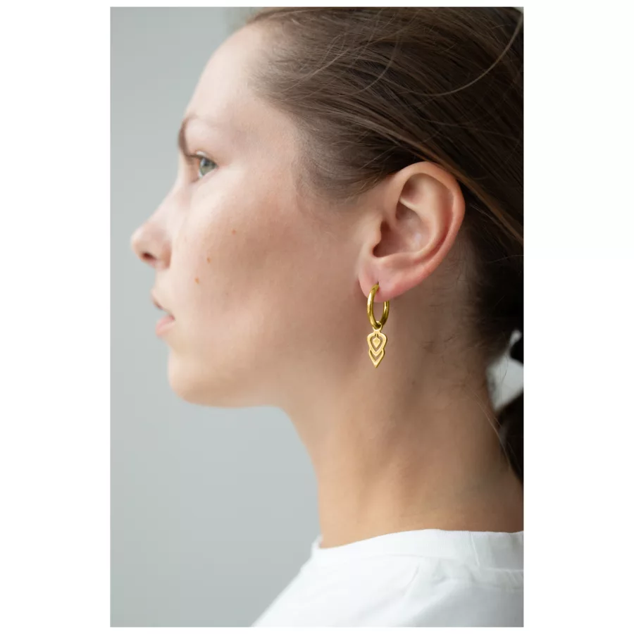 Frau mit goldenen Little Balisuta Hoops Ohrringen vor neutralem Hintergrund