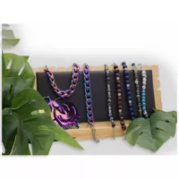 Schwarzes Ketten-Display mit Schmuck Schwarzes Kunstleder-Display mit bunten Halsketten auf Holz, umgeben von grünen Blättern