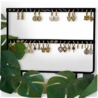 Schwarzes Ohrring-Display mit goldenen Ohrringen, umgeben von grünen Blättern