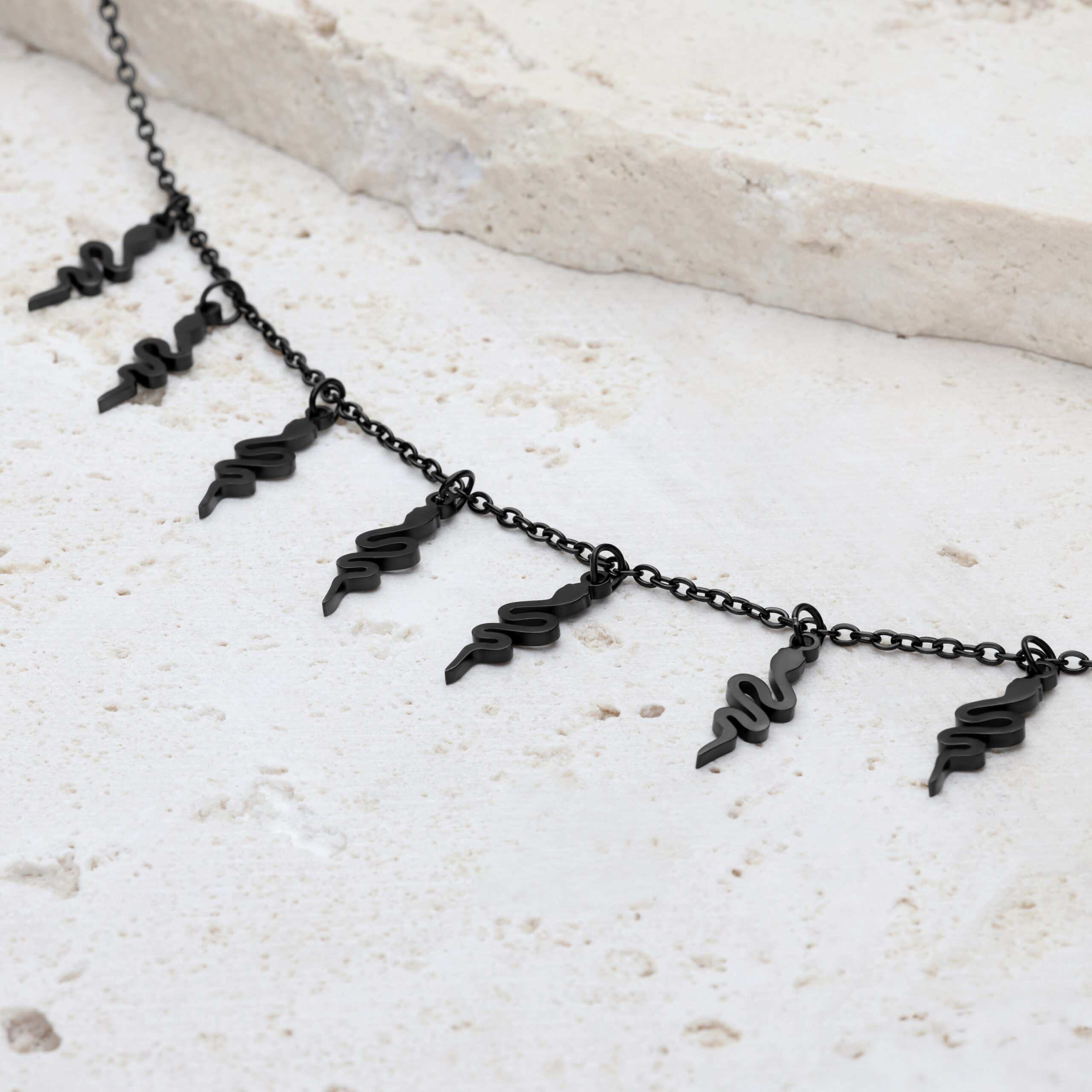 Schwarzes Snake Armband mit verstellbarem Verschluss auf hellem Stein