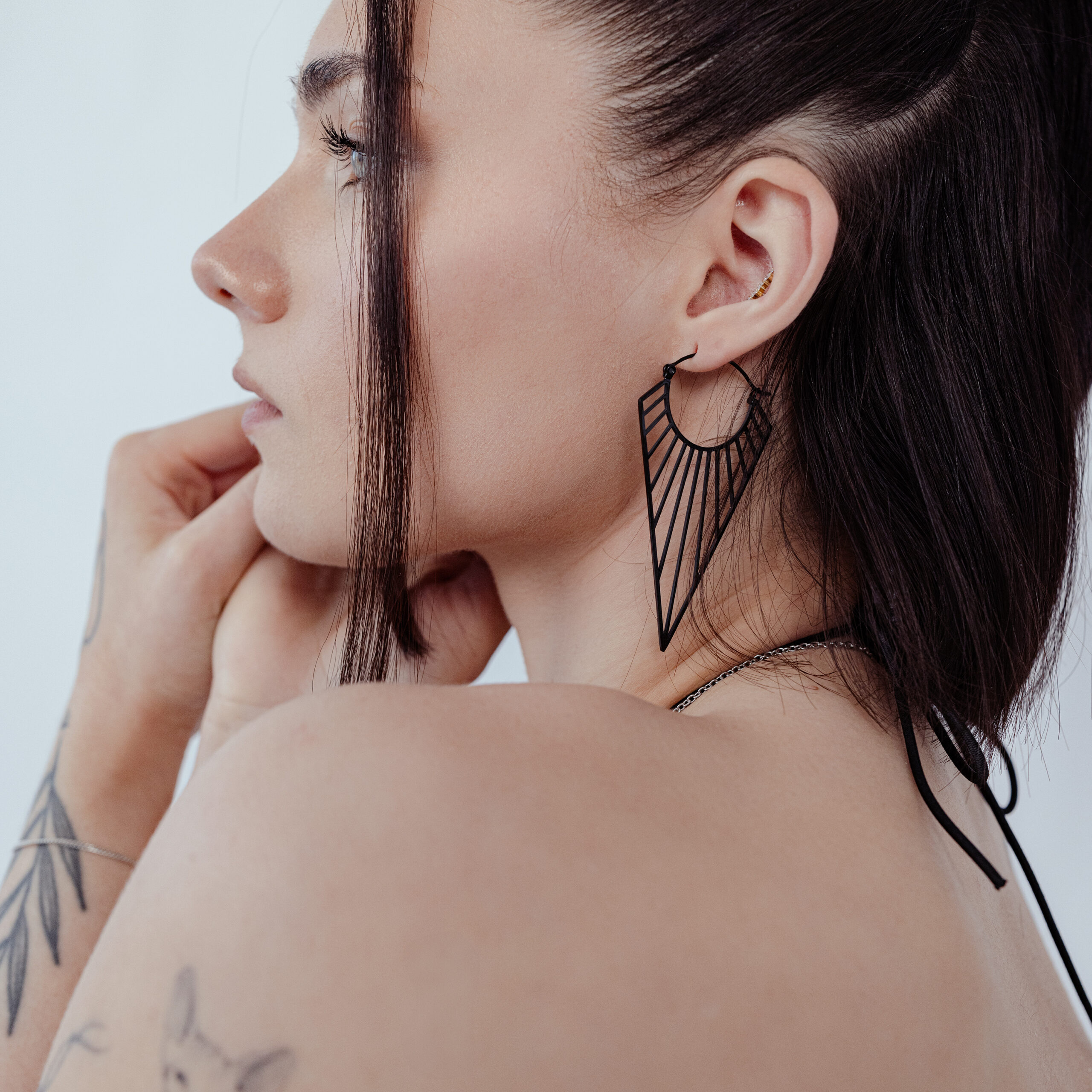 Prisma Hoops Ohrringe in Schwarz auf Frau Schwarze Prisma Hoops Ohrringe an einer Frau mit braunem Haar, seitlich fotografiert