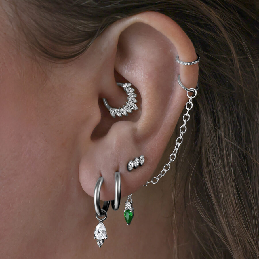 Mehrere Ohrringe im Ohr, darunter schwarze Little Tear Hoops mit grünem Kristall.