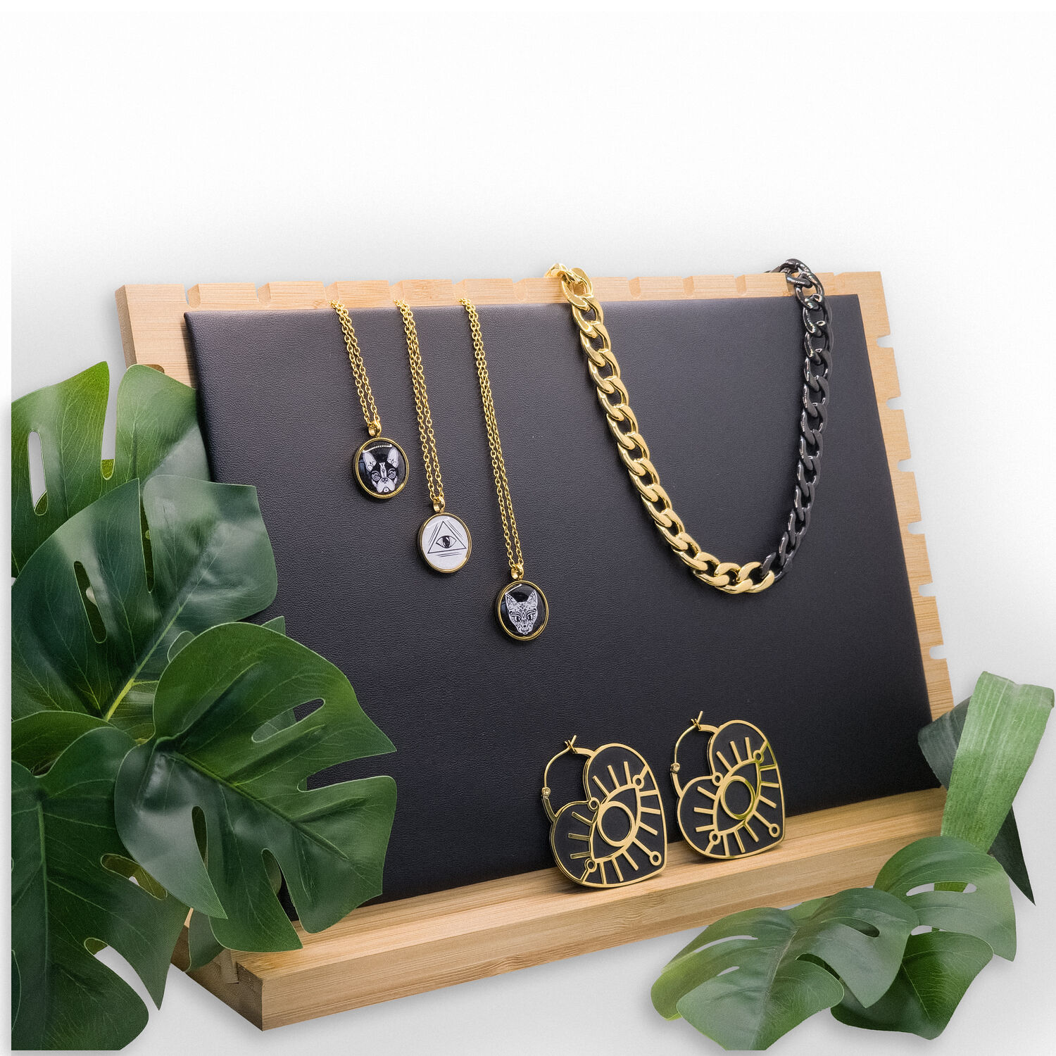 Schwarzer Schmuckdisplay mit goldenen Halsketten Schwarzer Display mit goldenen Ketten und Ohrringen auf Holzunterlage, umgeben von Pflanzen