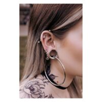 Stilvolle Ear Saddles in Silber und Schwarz Silberne und schwarze Ear Saddles an einem Ohr mit Piercings, Tattoo im Hintergrund