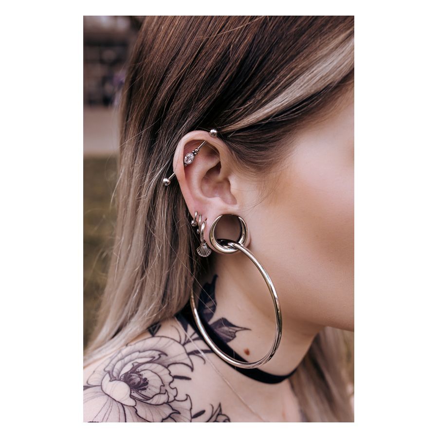 Stilvolle Ear Saddles in Silber und Schwarz Silberne und schwarze Ear Saddles an einem Ohr mit Piercings, Tattoo im Hintergrund