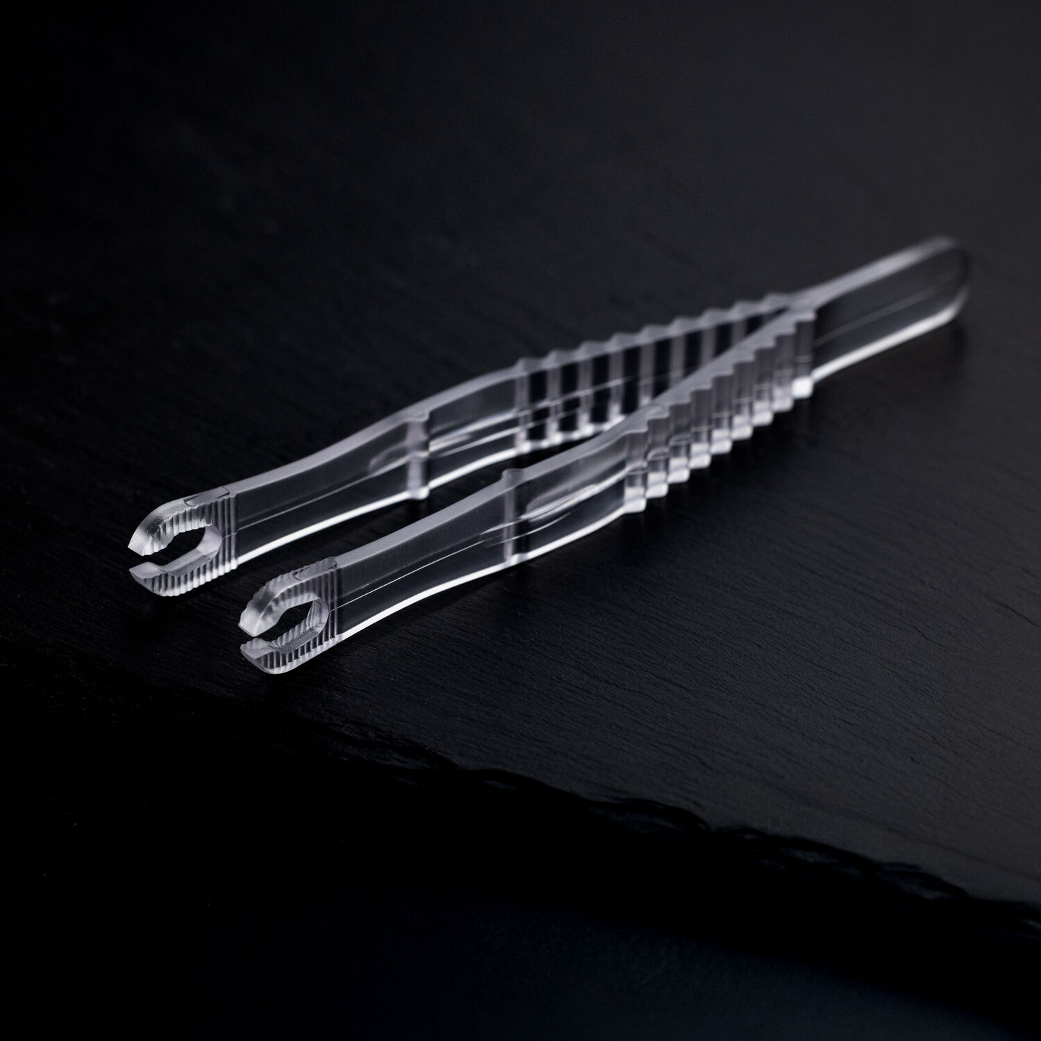 Sterile Runde Piercingzangen auf schwarzem Hintergrund Zwei transparente, sterile Runde Piercingzangen liegen überkreuzt auf einem dunklen Hintergrund.