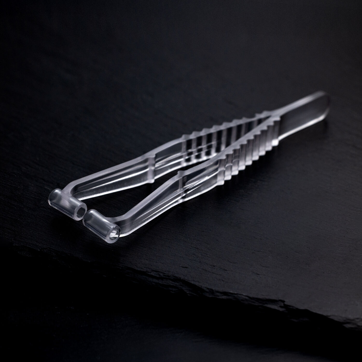 Sterile Septum Piercingzange auf schwarzem Hintergrund Transparente Septum Piercingzange aus Kunststoff auf dunklem, glattem Hintergrund